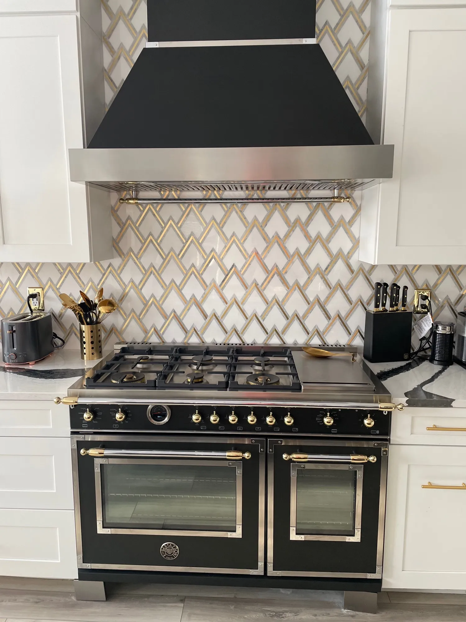 White marble and brass geometric backsplash behind a black-and-gold range
