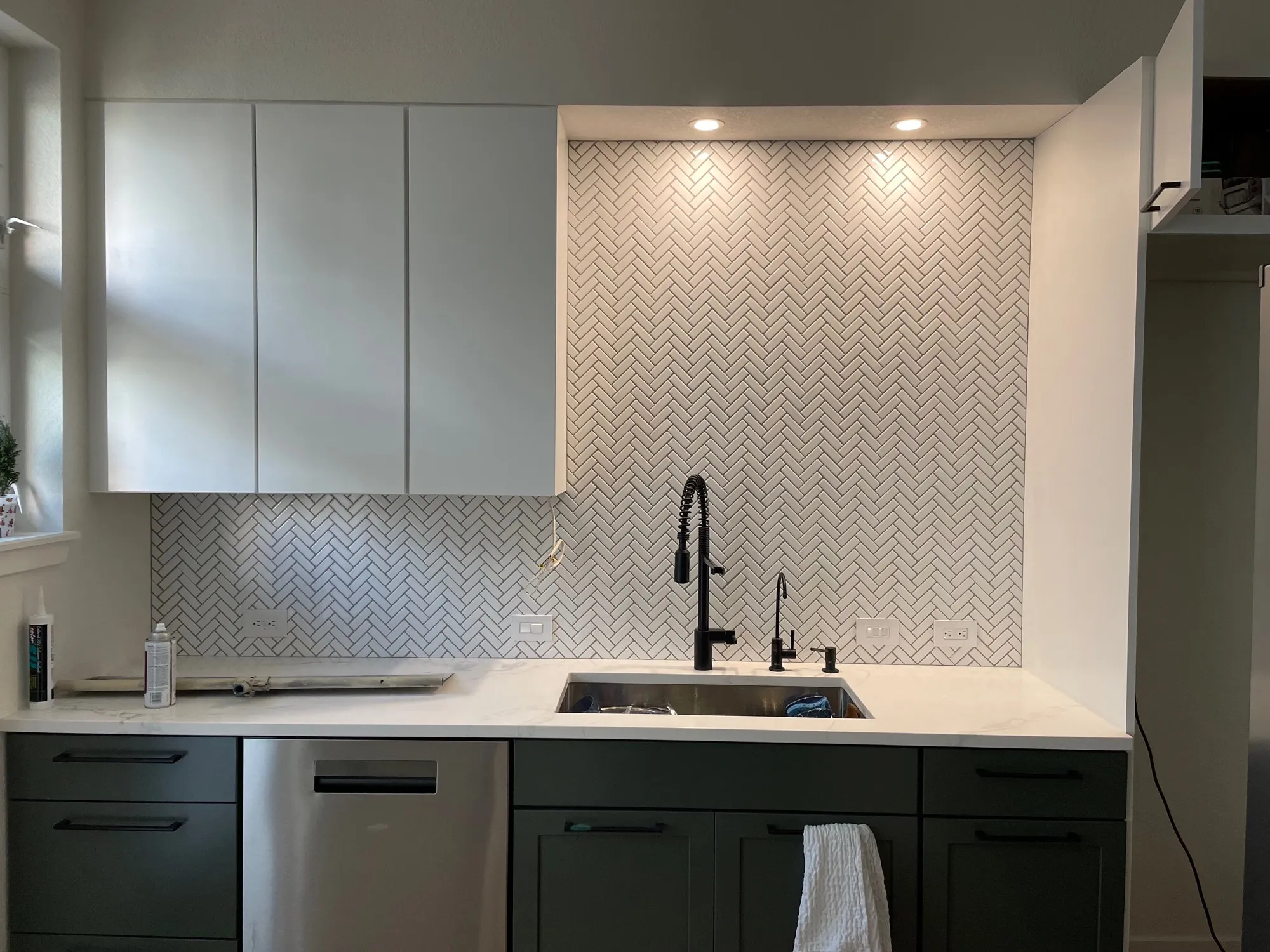 Full-height white herringbone mosaic backsplash with deep green cabinets