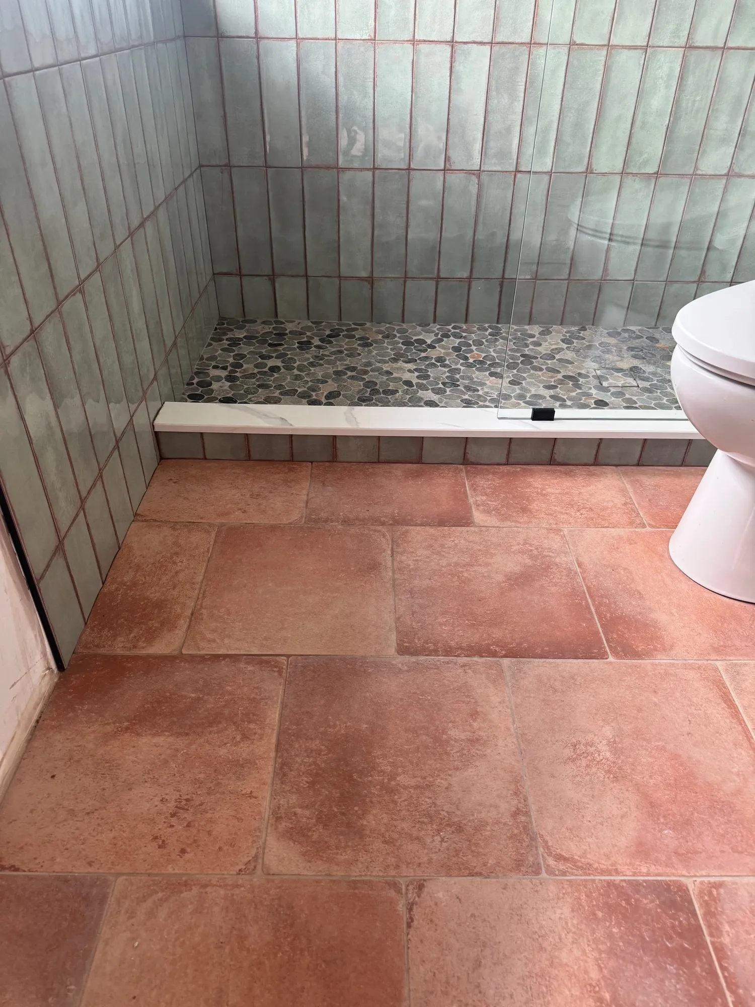 Shower detail with a black pebble pan meeting square terracotta floor tile