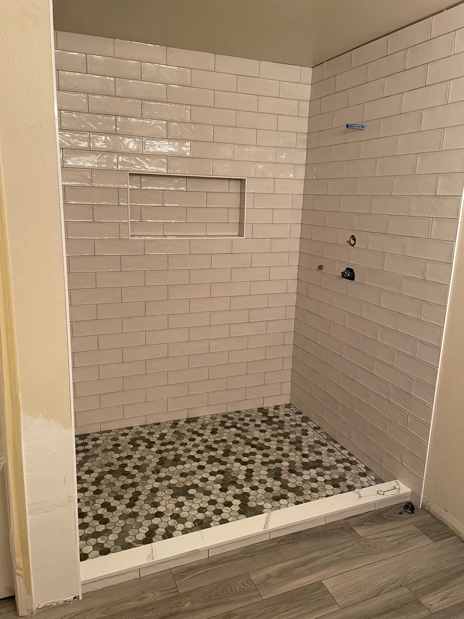 White subway tile shower with a niche and a gray hexagon mosaic floor