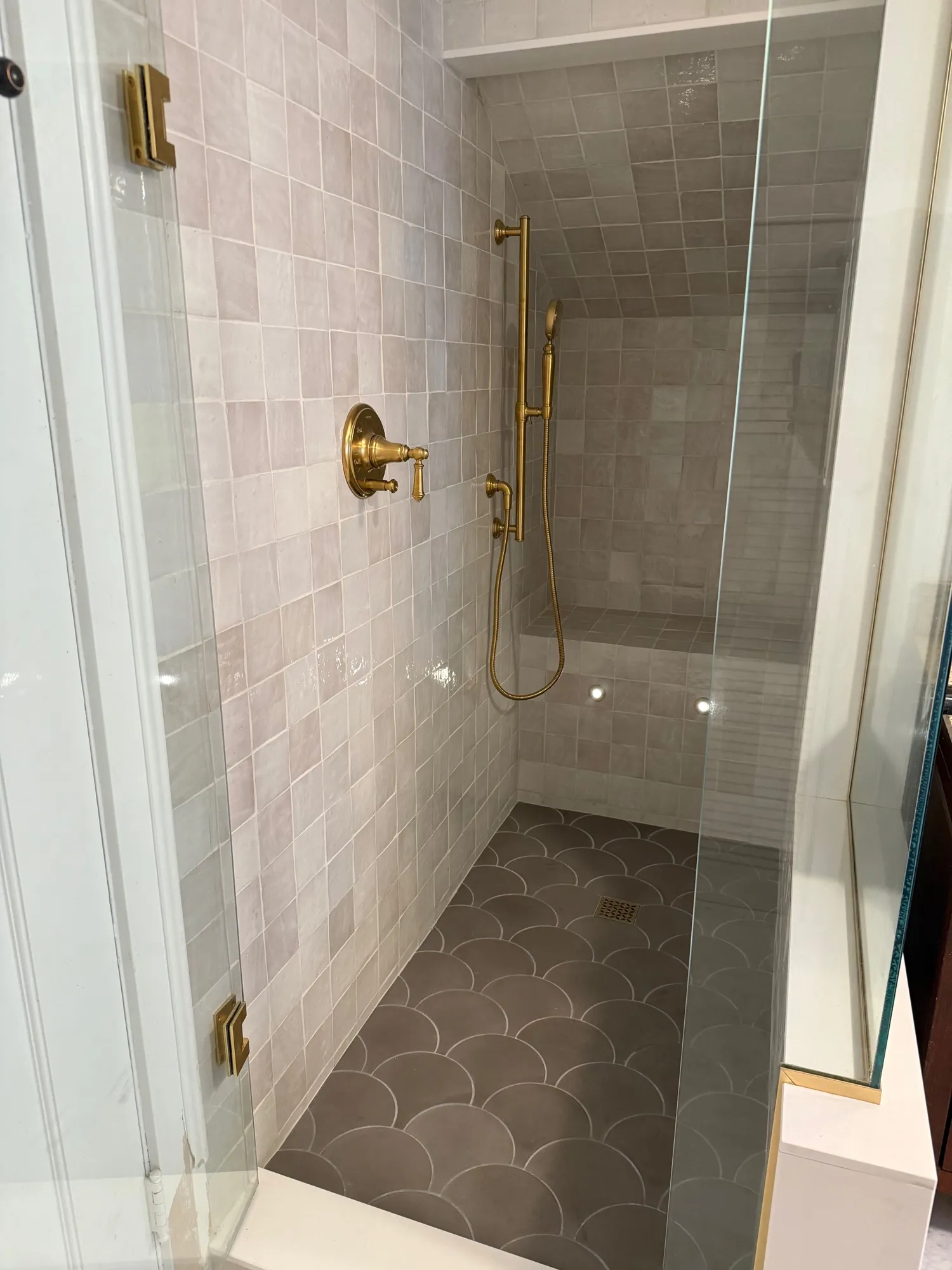 Walk-in shower in blush zellige tile with brass fixtures and a fish-scale floor