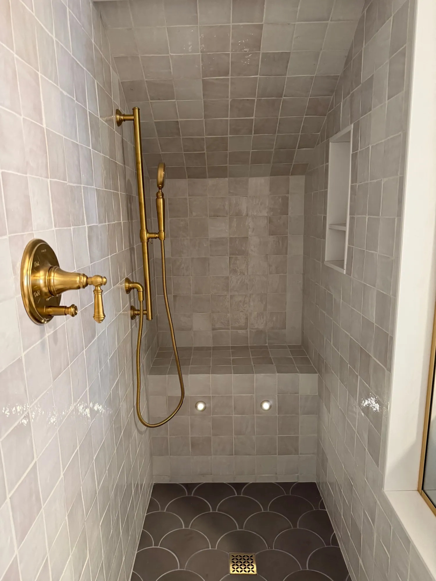 Walk-in shower in gray zellige tile with brass fixtures and a built-in bench
