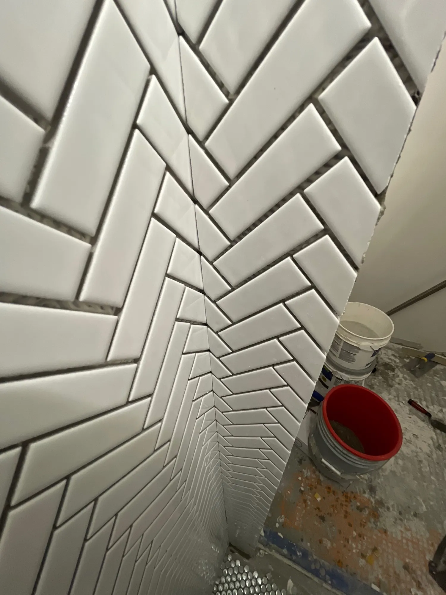 White subway tile set in a herringbone pattern on a shower wall